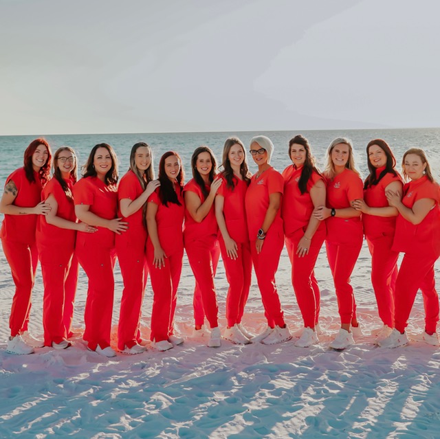 Photo of entire Nu-Smile team on the beach in coral colored scrub uniforms